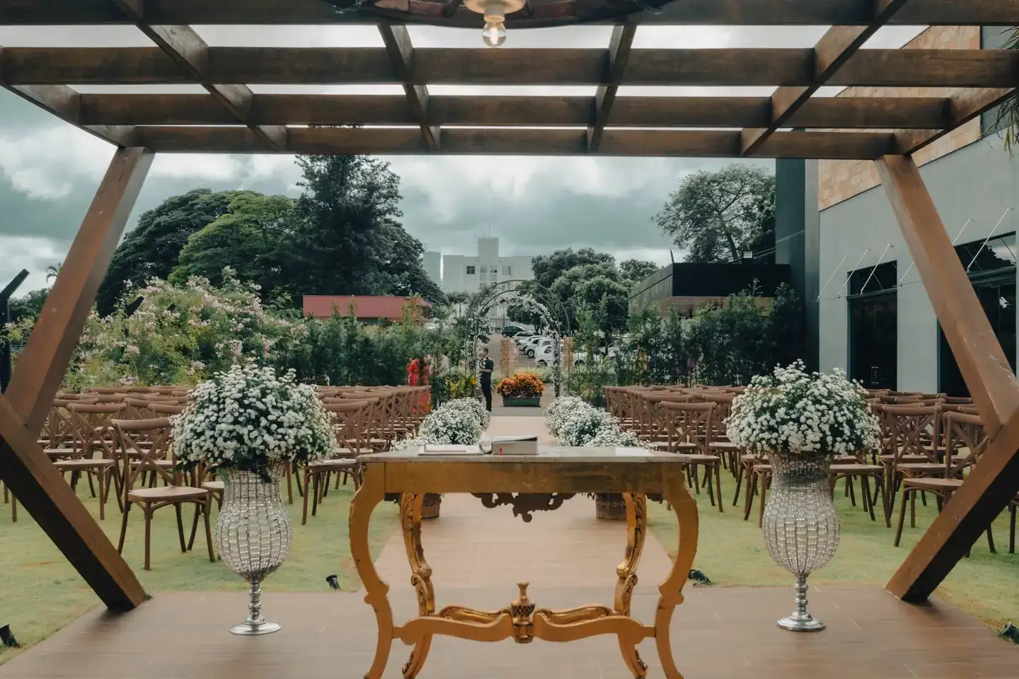 Cerimônia montada pela Totonho ao ar livre, com mesa provençal dourada, vasos de flores e fileiras de cadeiras de madeira
