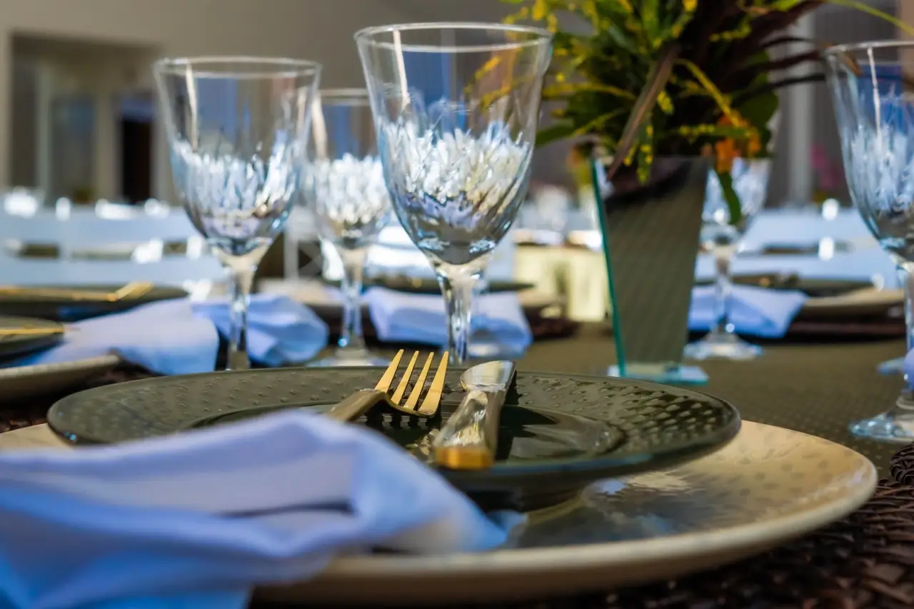 Taças de cristal lapidado sobre a mesa, ao lado de guardanapo azul claro dobrado sobre prato verde e talheres dourados