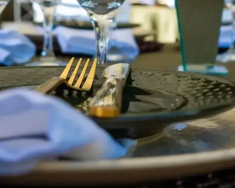 Garfo e faca dourados apoiados sobre um prato verde com guardanapo de tecido azul claro