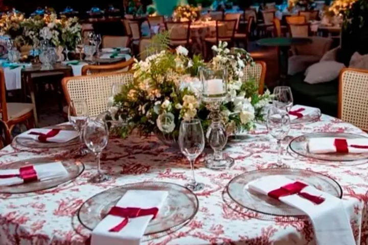 Mesa redonda com toalha Toile de Jouy bordô, sousplat de cristal e guardanapos brancos com laço bordô