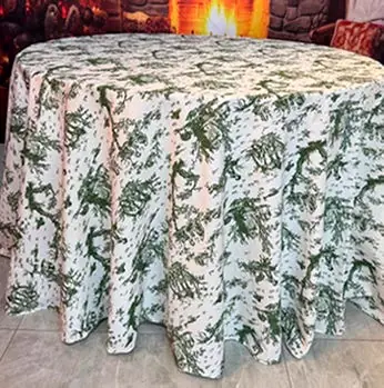 Mesa redonda coberta por toalha com estampa Toile de Jouy verde sobre fundo branco, com caimento até o chão